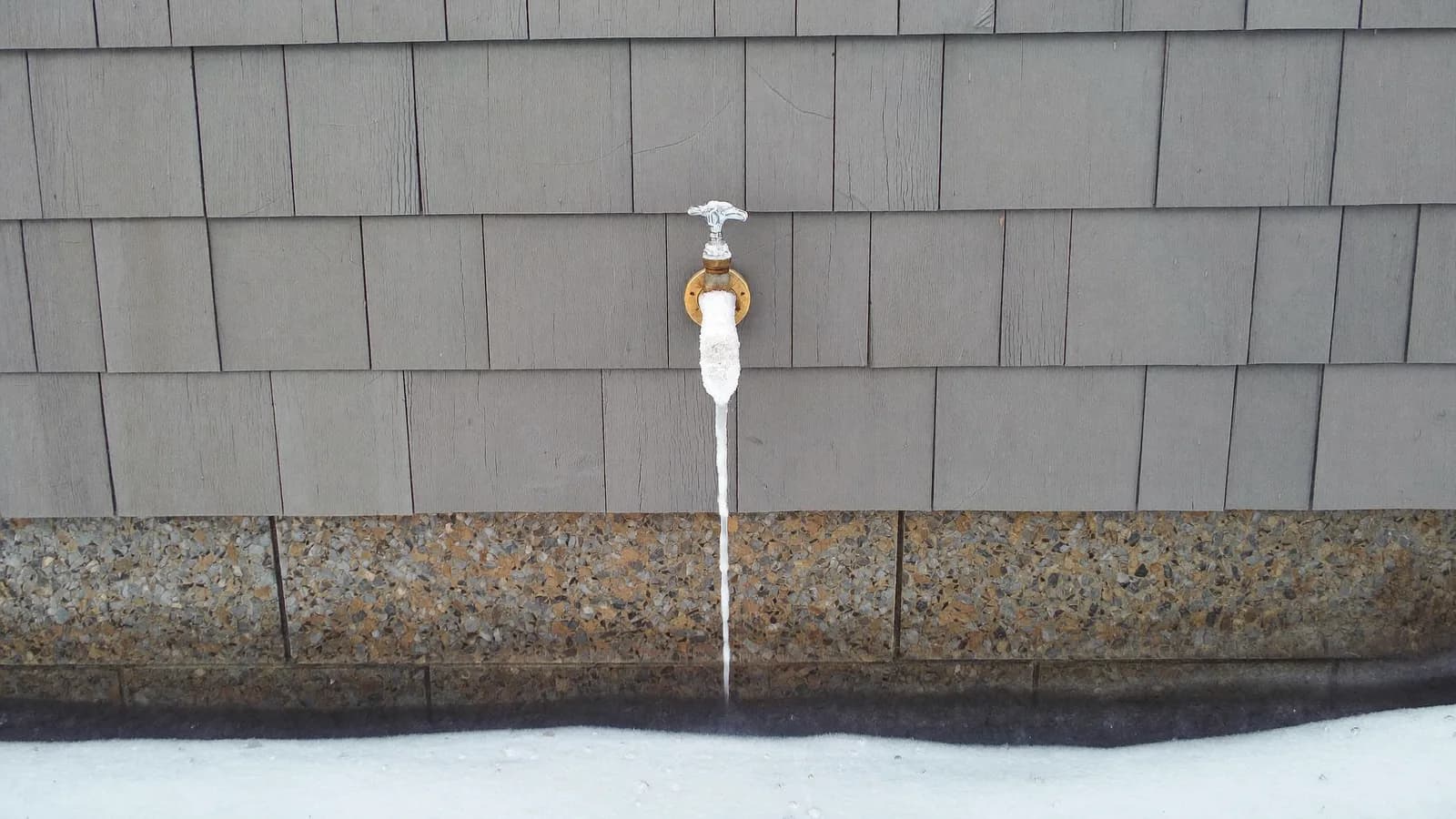 Frost-covered outdoor spigot with an icicle on a cedar shingle house during a Massachusetts cold snap